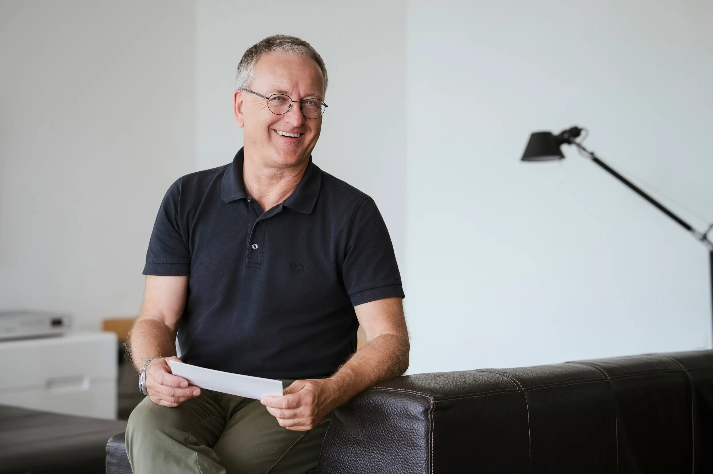 Richard Zauner sitzt auf der Couch, Unterlagen in der Hand, lächelt in die Kamera – persönliches Verkaufstraining auf Augenhöhe